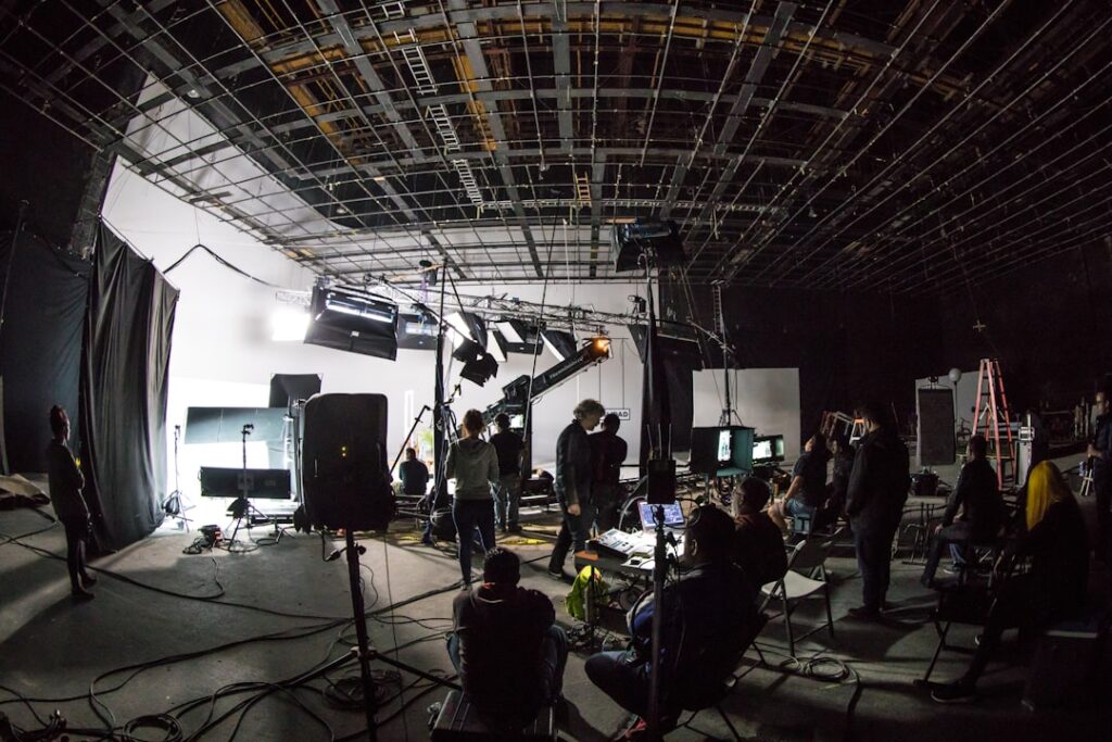 A film crew working on a large soundstage with lighting equipment and cameras