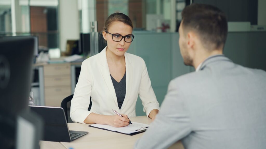 Woman in glasses interviews man at office desk